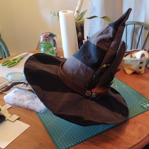 A gray and black striped witch har with a leather band and feathers sticking out. 